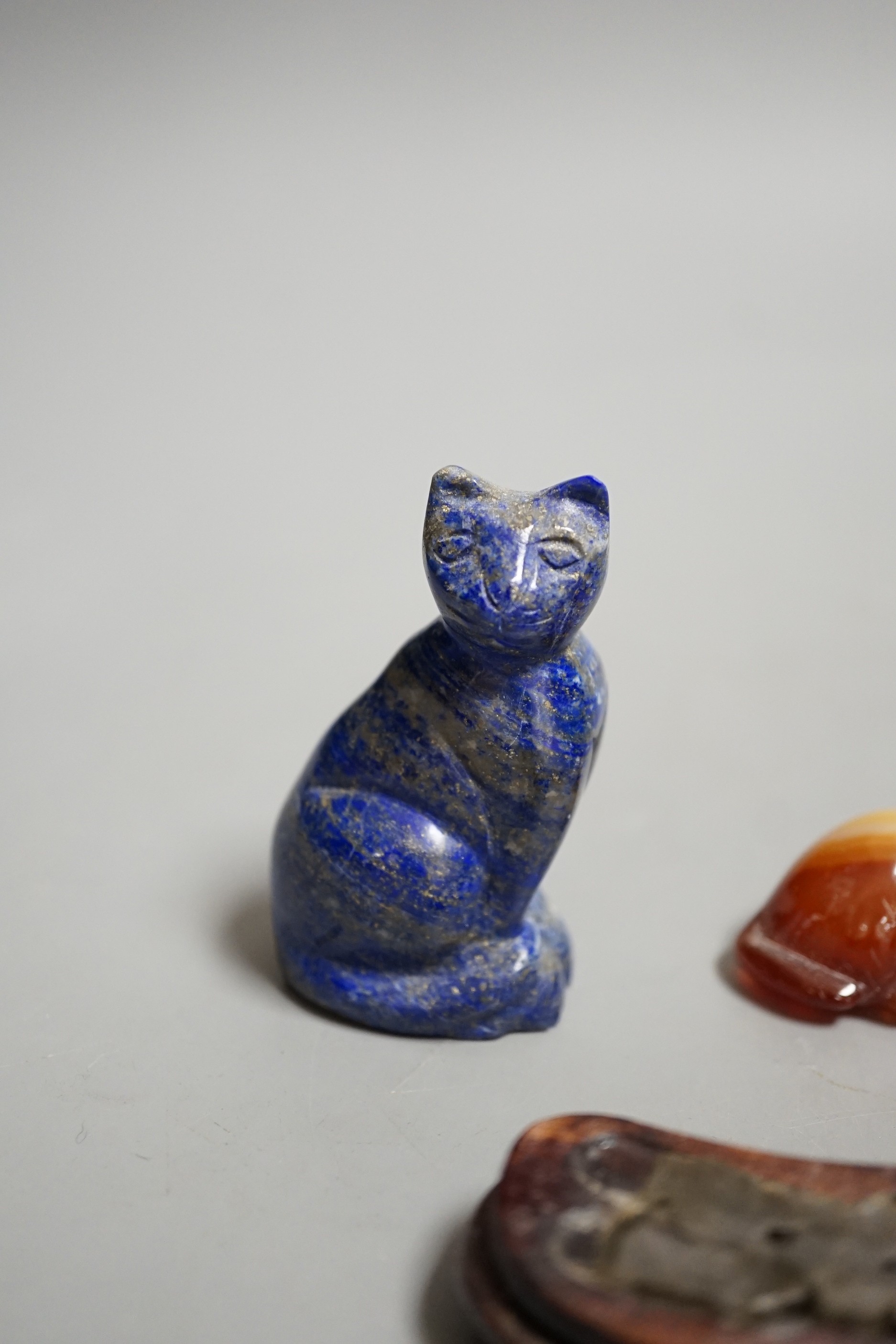 A Chinese carved lapis lazuli seated cat, a banded agate recumbent cat on hardwood stand and a white metal mounted agate scent bottle